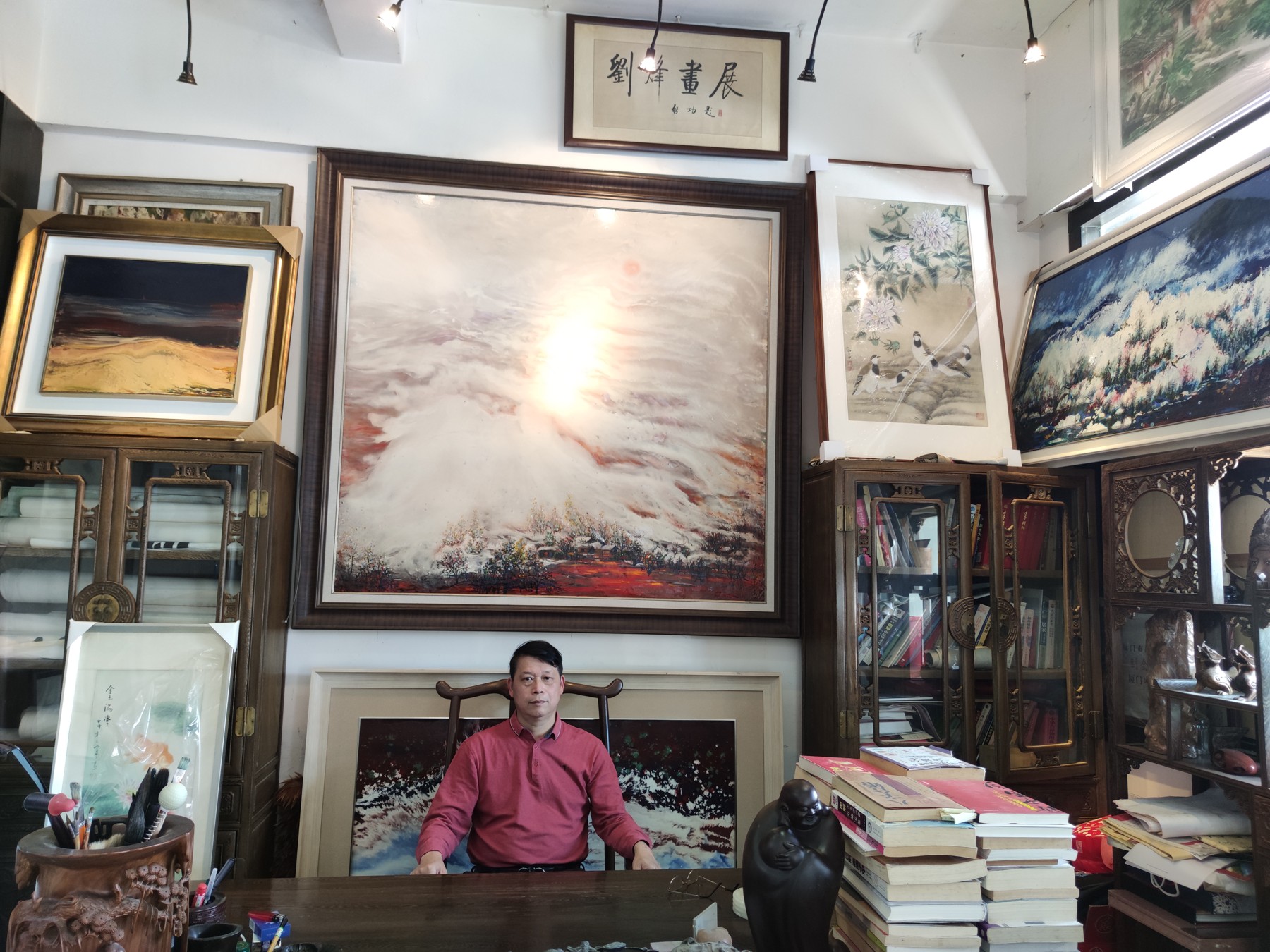 刘烽坐在画廊中,身后陈列作品与书籍